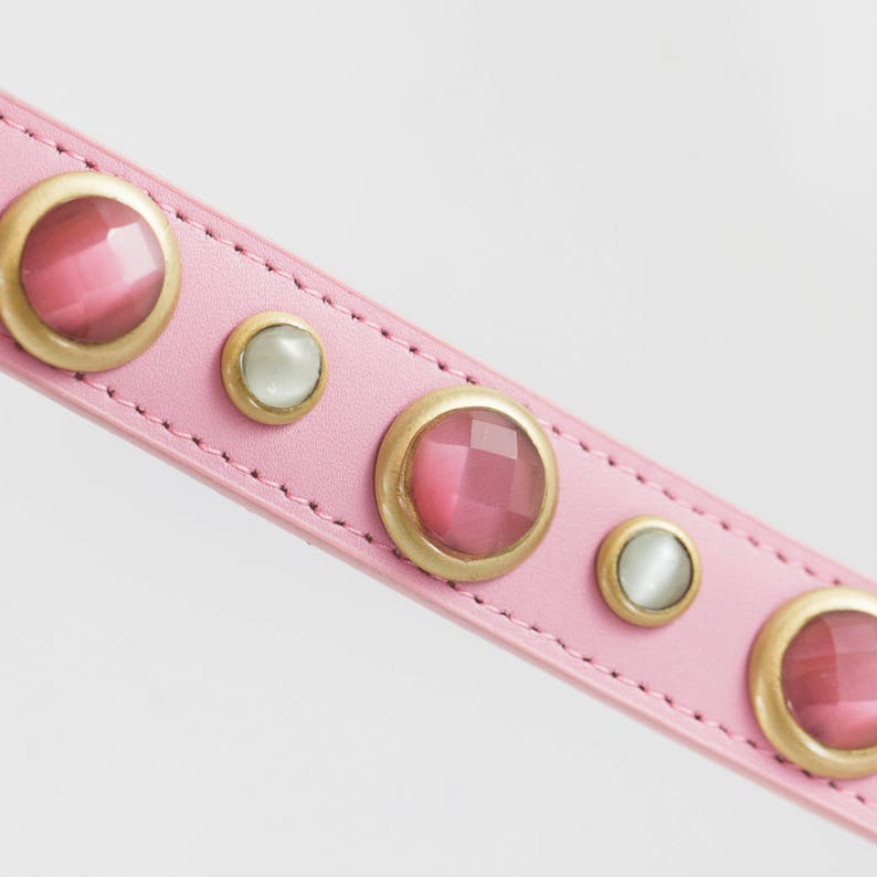 Op de afbeelding: Roze leren hondenhalsband met gouden accenten en roze en witte edelstenen.