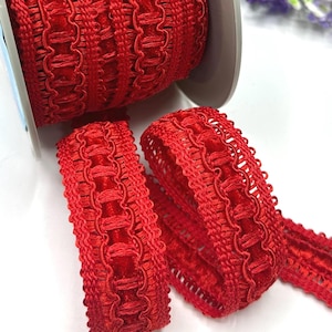 May include: A reel of vibrant red decorative trim with a woven pattern. Two smaller sections of the same trim are unrolled, displaying the intricate design. The trim is suitable for sewing, crafting, or adding embellishments to various projects.