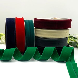 Peut inclure: Assortiment de ruban de velours de différentes couleurs, notamment bleu marine, rouge, vert et bordeaux. Le ruban est empilé en un tas, avec un ruban vert enroulé au premier plan.