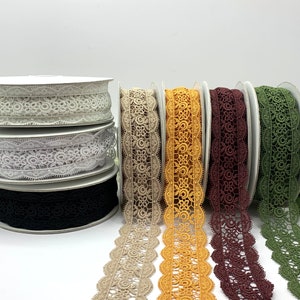 May include: Five spools of decorative lace trim in various colors, including beige, yellow, burgundy, and green. The lace trim has a scalloped edge and a delicate floral pattern.