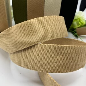 May include: Close-up of a beige cotton webbing strap. The strap is woven with a textured pattern and is rolled up. The strap is part of a set of different colored straps.