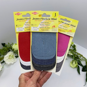 May include: Three packs of denim patches for repairing jeans. Each pack contains three patches in different colors: red, blue, and pink. The packaging is yellow and features the text "Jeans-Flecken Mini" and "zum Ausbessern und Verst&auml;rken".