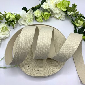 May include: A roll of off-white cotton webbing, a type of flat woven fabric used for straps, belts, and other applications.