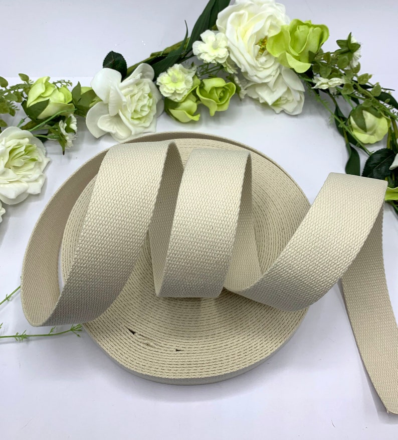 May include: A roll of off-white cotton webbing, a type of flat woven fabric used for straps, belts, and other applications.