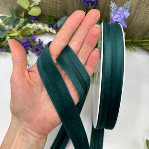 K&ouml;nnte beinhalten: Eine Spule mit dunkelgr&uuml;nem Samtband mit Satin-Finish. Das Band ist etwa 2,5 cm breit und wird auf einer wei&szlig;en Spule gezeigt.