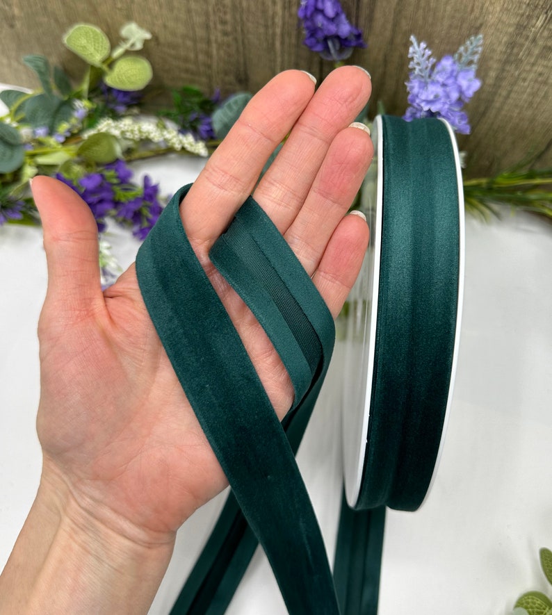 K&ouml;nnte beinhalten: Eine Spule mit dunkelgr&uuml;nem Samtband mit Satin-Finish. Das Band ist etwa 2,5 cm breit und wird auf einer wei&szlig;en Spule gezeigt.