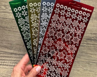 Foglio di adesivi a specchio con fiocchi di neve nei colori verde, rosso, oro e argento metallizzato per lavoretti natalizi.