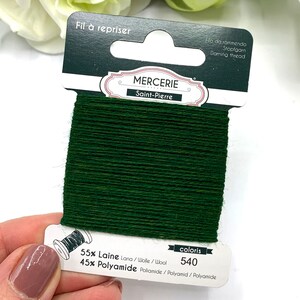 May include: A spool of dark green darning thread labeled "Mercerie Saint-Pierre" with the text "Fil &agrave; repriser" and "coloris 540". The thread is 55% wool and 45% polyamide.