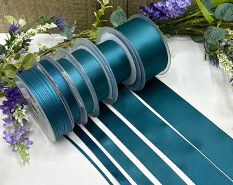 May include: Assortment of teal satin ribbon spools in various widths. The ribbon is wound around spools and laid out flat on a white surface.