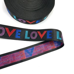May include: Black webbing with the word "LOVE" printed in rainbow colors. The webbing has a glittery red and blue pattern on the back.