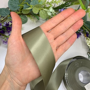 May include: A roll of sage green satin ribbon. The ribbon is 1 inch wide and has a slight sheen.