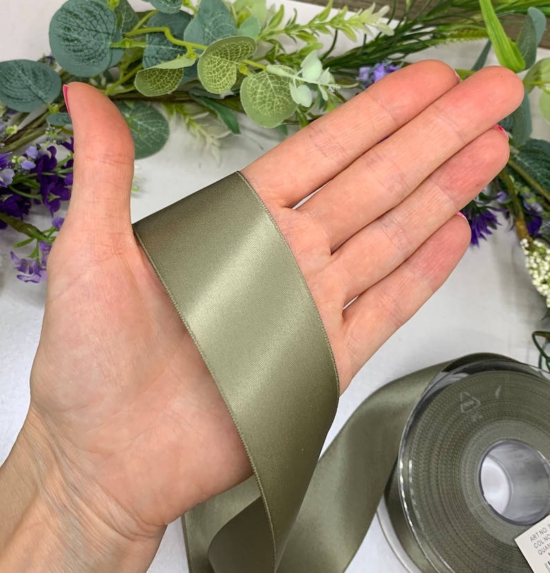 May include: A roll of sage green satin ribbon. The ribbon is 1 inch wide and has a slight sheen.