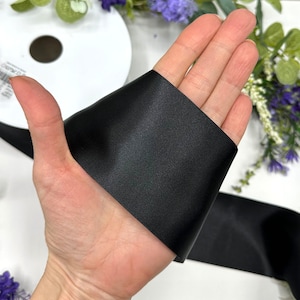 May include: A hand holding a black satin ribbon. The ribbon is folded in half and the hand is holding the folded edge.