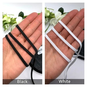 May include: Two spools of elastic cord, one black and one white. The elastic cord is shown wrapped around a hand.
