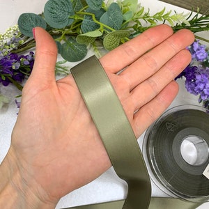 May include: A roll of olive green satin ribbon. The ribbon is 1 inch wide and has a smooth, silky texture.