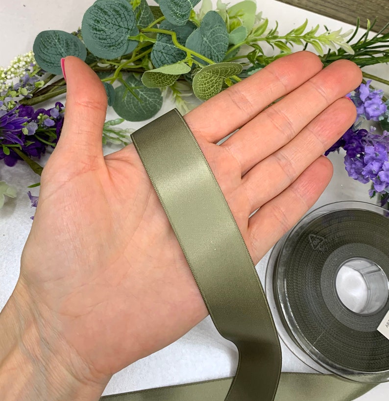 May include: A roll of olive green satin ribbon. The ribbon is 1 inch wide and has a smooth, silky texture.