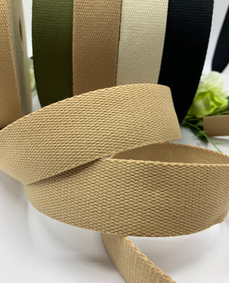 May include: Close-up of a beige cotton webbing strap. The strap is woven with a textured pattern and is rolled up. The strap is part of a set of different colored straps.