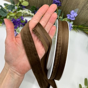 K&ouml;nnte beinhalten: Eine Spule mit braunem Samtband. Das Band ist etwa 2,5 cm breit und hat eine weiche, pl&uuml;schige Textur.