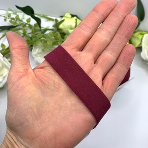 Puede incluir: Primer plano de una banda el&aacute;stica de color granate, de aproximadamente 2,5 cm de ancho, que se muestra en una mano.