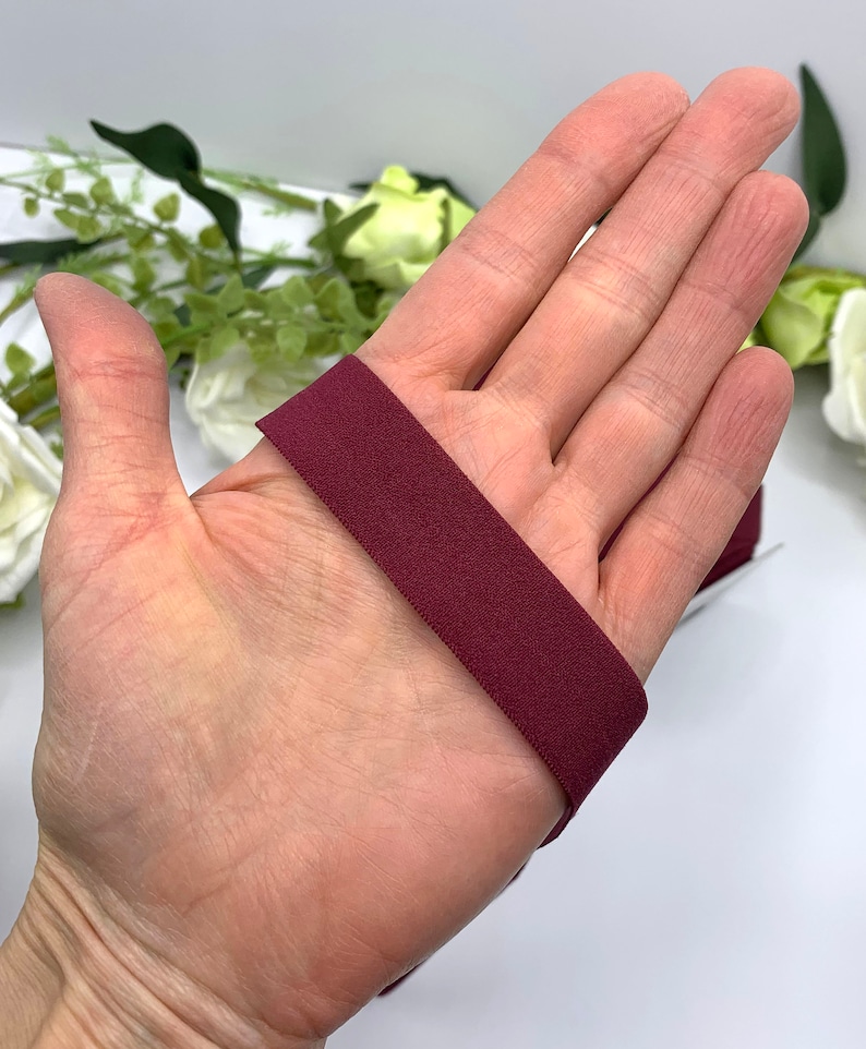Puede incluir: Primer plano de una banda el&aacute;stica de color granate, de aproximadamente 2,5 cm de ancho, que se muestra en una mano.