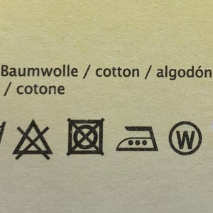 May include: A white tag with black text and symbols. The text reads "100% Baumwolle / cotton / algod&oacute;n / coton / cotone". The symbols are for washing, drying, ironing, and recycling.