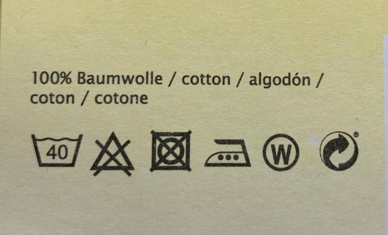 May include: A white tag with black text and symbols. The text reads "100% Baumwolle / cotton / algod&oacute;n / coton / cotone". The symbols are for washing, drying, ironing, and recycling.