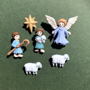 May include: A set of miniature Christmas figurines. The set includes a shepherd with a staff, a girl holding a lamb, an angel with wings, a star, and two sheep. The figurines are in blue, white, and tan.