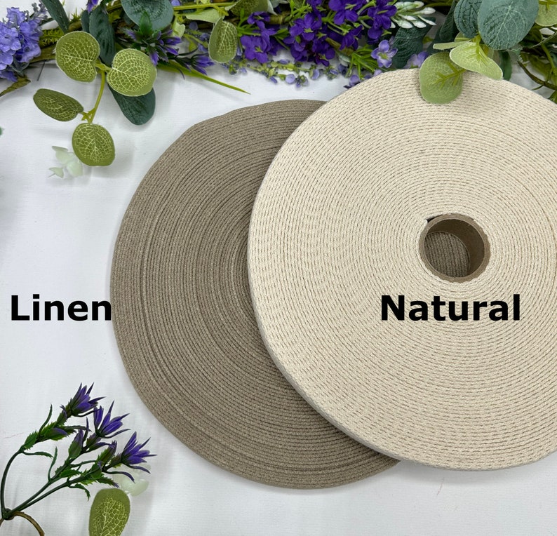 May include: Two spools of woven fabric ribbon, one in a natural off-white color and the other in a linen-colored shade of gray. The word "Natural" is printed on the right spool, and "Linen" is printed on the left spool.