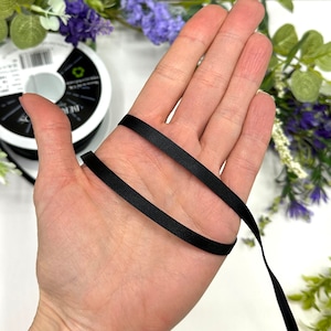 May include: A black satin ribbon is wrapped around a hand. The ribbon is smooth and shiny.