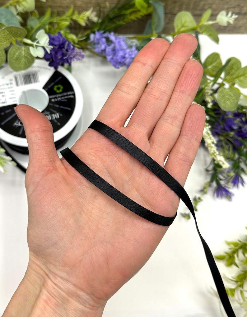 May include: A black satin ribbon is wrapped around a hand. The ribbon is smooth and shiny.
