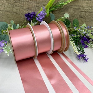 May include: Four spools of rose gold satin ribbon. The ribbon is arranged in a line with the spools at the top and the ribbon extending out to the bottom.