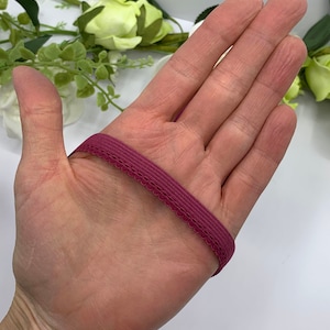 Puede incluir: Primer plano de una banda el&aacute;stica de color burdeos con un borde festoneado. La banda est&aacute; sobre la mano de una persona.