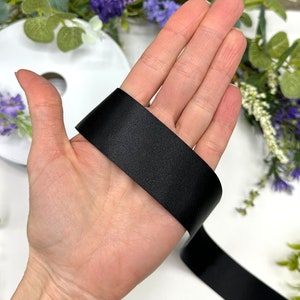 May include: A close-up of a black satin ribbon, shown on a hand. The ribbon is smooth and shiny.