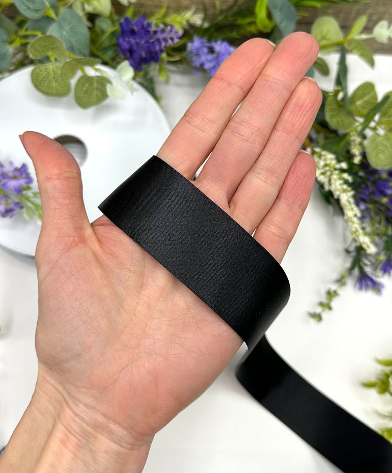 May include: A close-up of a black satin ribbon, shown on a hand. The ribbon is smooth and shiny.