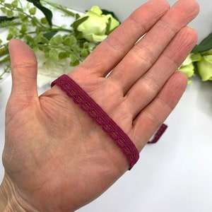 Puede incluir: Primer plano de una cinta de encaje el&aacute;stica de color burdeos con un borde festoneado.