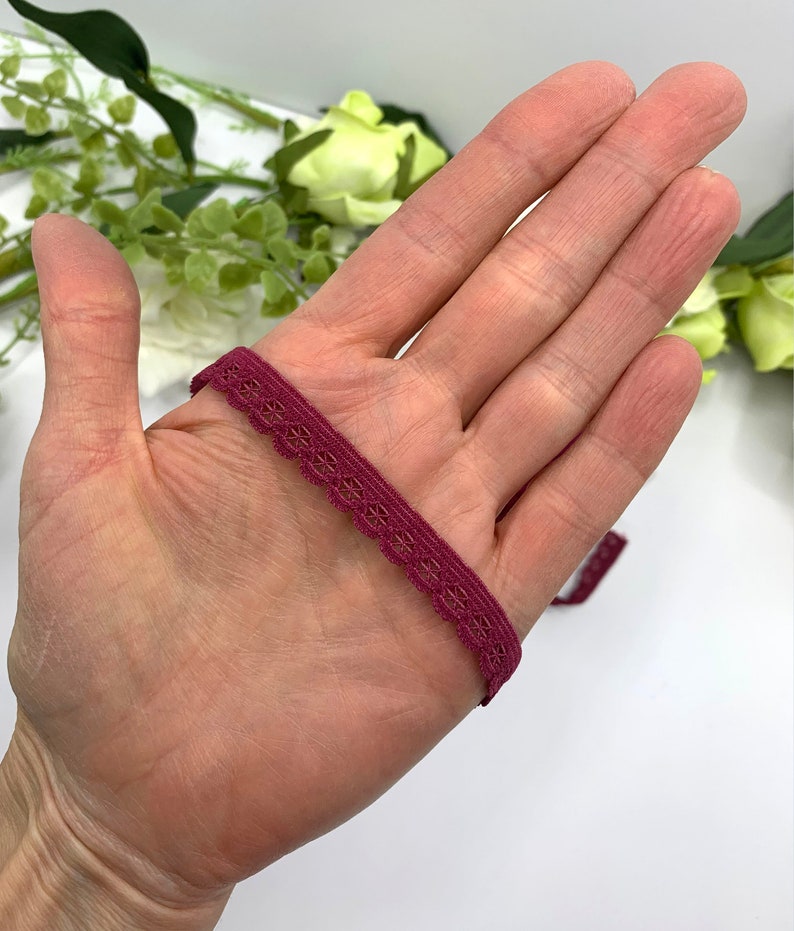 Puede incluir: Primer plano de una cinta de encaje el&aacute;stica de color burdeos con un borde festoneado.