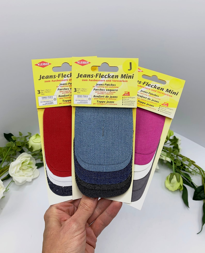 May include: Three packs of denim patches for repairing jeans. Each pack contains three patches in different colors: red, blue, and pink. The packaging is yellow and features the text "Jeans-Flecken Mini" and "zum Ausbessern und Verst&auml;rken".