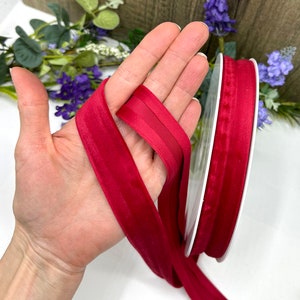 K&ouml;nnte beinhalten: Eine Spule mit rotem Samtband mit Satin-Finish. Das Band ist etwa 2,5 cm breit und wird auf einer wei&szlig;en Spule gezeigt.