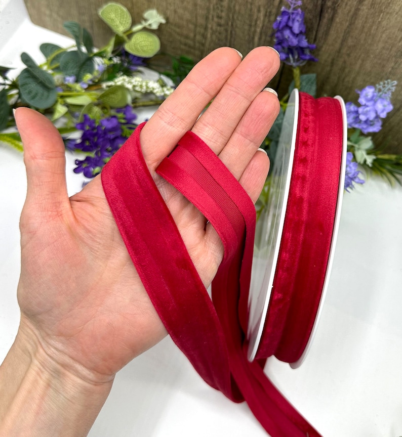K&ouml;nnte beinhalten: Eine Spule mit rotem Samtband mit Satin-Finish. Das Band ist etwa 2,5 cm breit und wird auf einer wei&szlig;en Spule gezeigt.