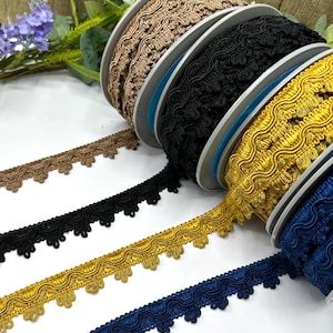 May include: A selection of decorative trim on spools, featuring colours such as gold, black, and navy. The trim has a scalloped edge and is made from woven material. Some trim is unrolled, showcasing the design.