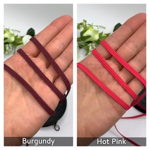 May include: Two close-up images of elastic cord, one burgundy and one hot pink. The cord is shown folded in thirds and is approximately 1/2 inch wide.