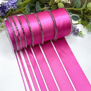 May include: A roll of bright fuchsia satin ribbon with a glossy finish. The ribbon is displayed with several parallel strips of the same colour, creating a visually appealing pattern. The ribbon is ideal for crafts, gift wrapping, and decorative projects.