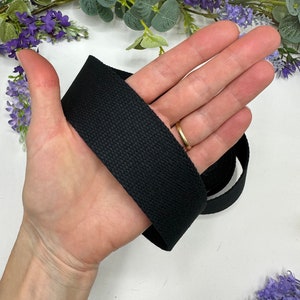 May include: Black cotton webbing strap, approximately 1 inch wide, shown wrapped around a hand.
