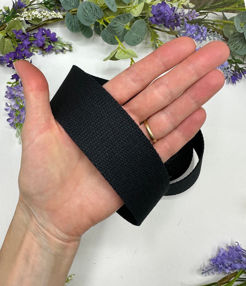 May include: Black cotton webbing strap, approximately 1 inch wide, shown wrapped around a hand.