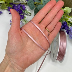 May include: A spool of dusty rose satin ribbon. The ribbon is 3mm wide and is shown wrapped around a hand.
