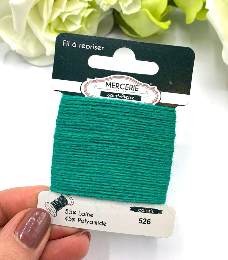 May include: A spool of green embroidery floss with the text "Fil &agrave; repriser" and "Mercerie Saint-Pierre" on the label. The label also indicates the floss is 55% wool and 45% polyamide and the color number is 526.