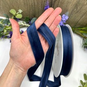 K&ouml;nnte beinhalten: Eine Spule mit marineblauem Satinband mit Samtkante. Das Band ist etwa 2,5 cm breit.