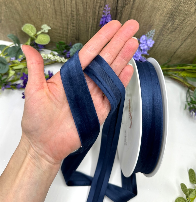 K&ouml;nnte beinhalten: Eine Spule mit marineblauem Satinband mit Samtkante. Das Band ist etwa 2,5 cm breit.