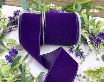 Puede incluir: Dos carretes de cinta de terciopelo morado oscuro con borde de satén. La cinta está enrollada en carretes blancos.