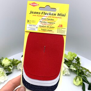 May include: A pack of three iron-on patches for repairing jeans. The patches are red, white, and blue denim. The packaging is yellow and has the text "Jeans-Flecken Mini" and "zum Ausbessern und Verst&auml;rken".